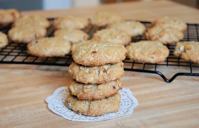 photo of cookies on a white doily on a wooden board with other cookies on a bakers rack in the background