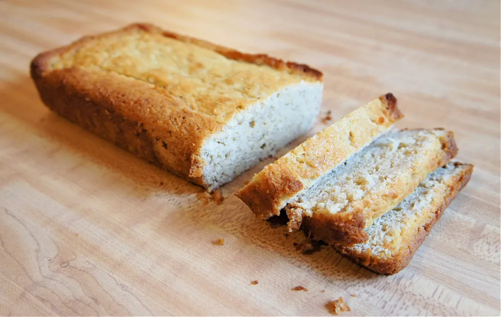 Loaf of Coconut Banana Bread sliced on a wooden cutting board