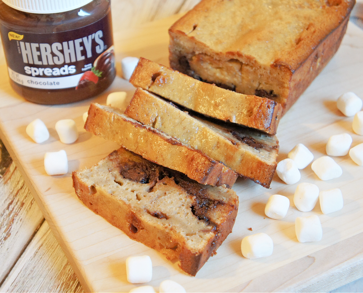 Rocky Road Banana Bread with a jar of hersheys chocolate spreads and mini marshmallows ona wooden cutting board
