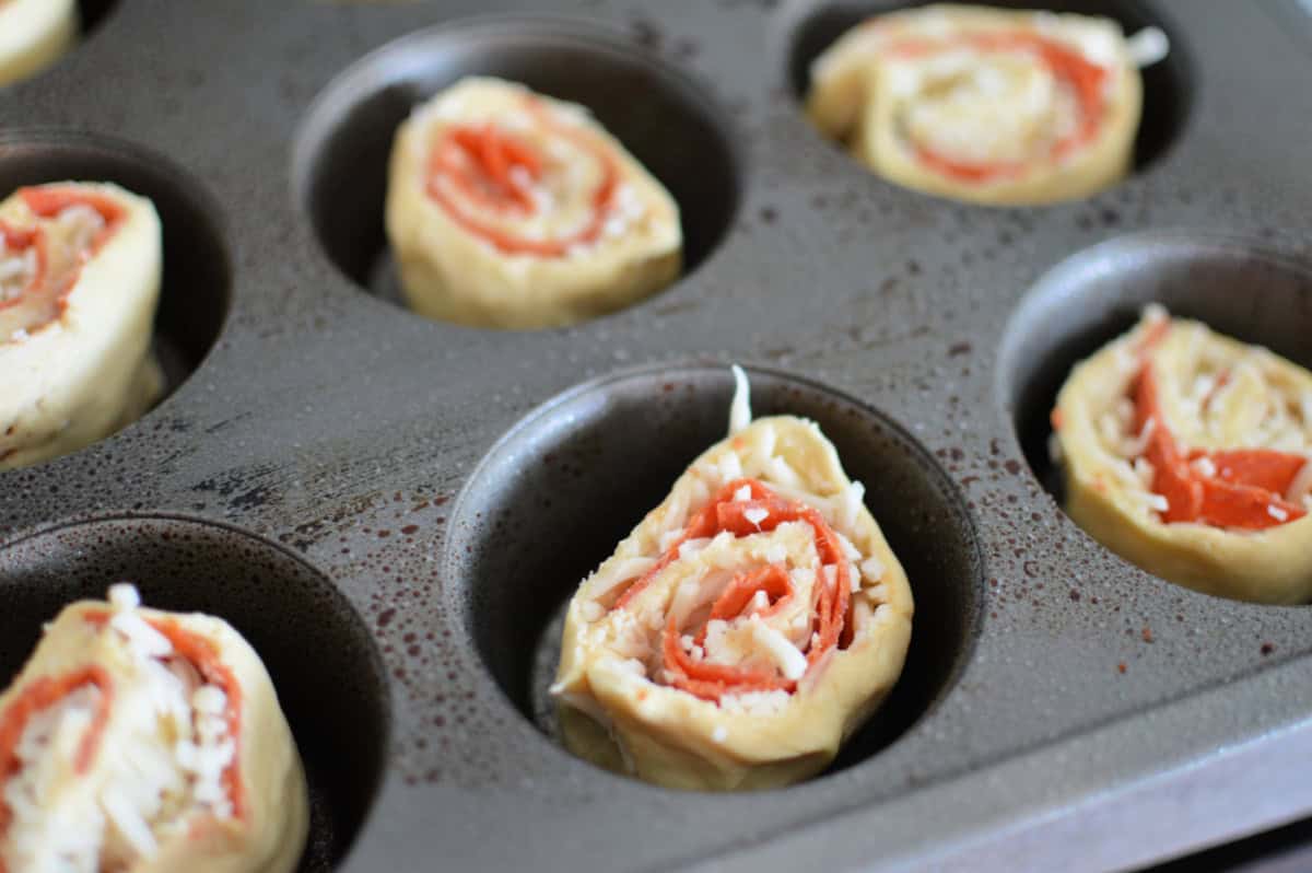 muffin tin filled with puffy pastry, cheese and pepperoni