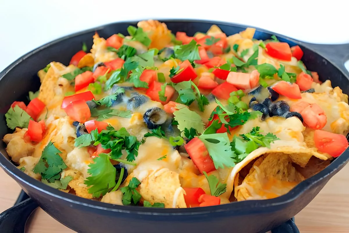 cast iron pan filled with tortilla chips, chicken, tomatoes, cheese and olives
