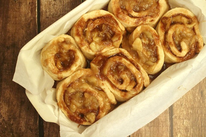 rolls with cinnamon sugar and apples in a baking dish lined with parchment paper