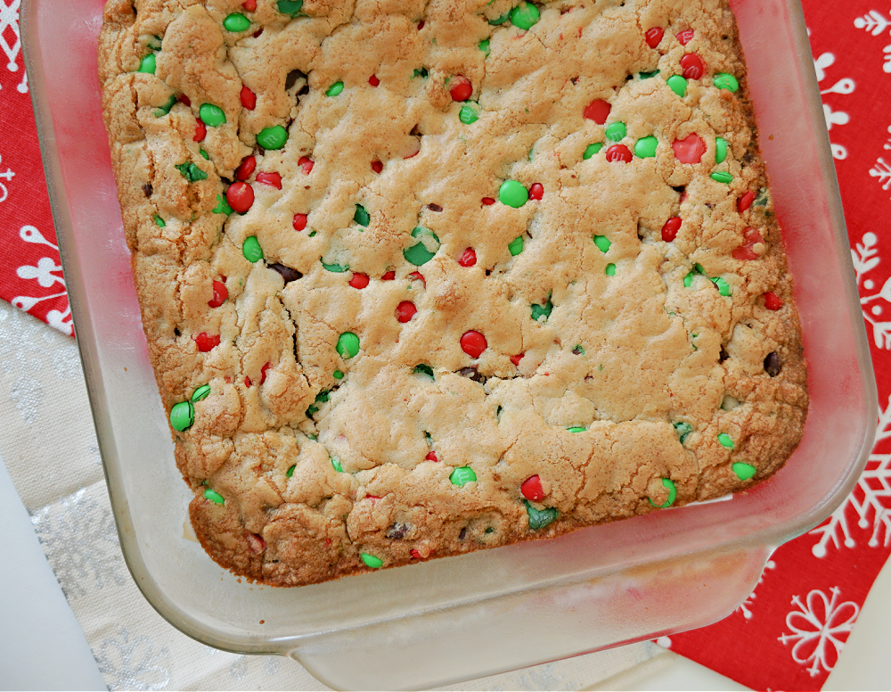 a baking dish filled with cookies bars with red and green M&Ms and chocolate chips