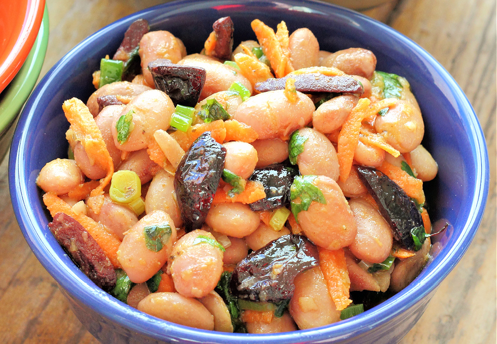 A bowl of bean salad with fried kalamata olives.