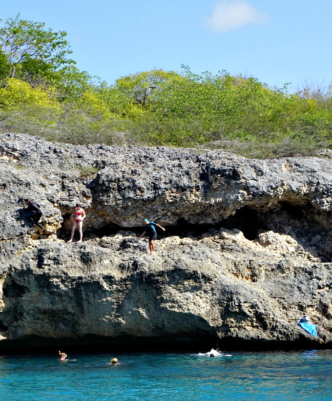 children and teenager diving off of a rocky cliff in curacao