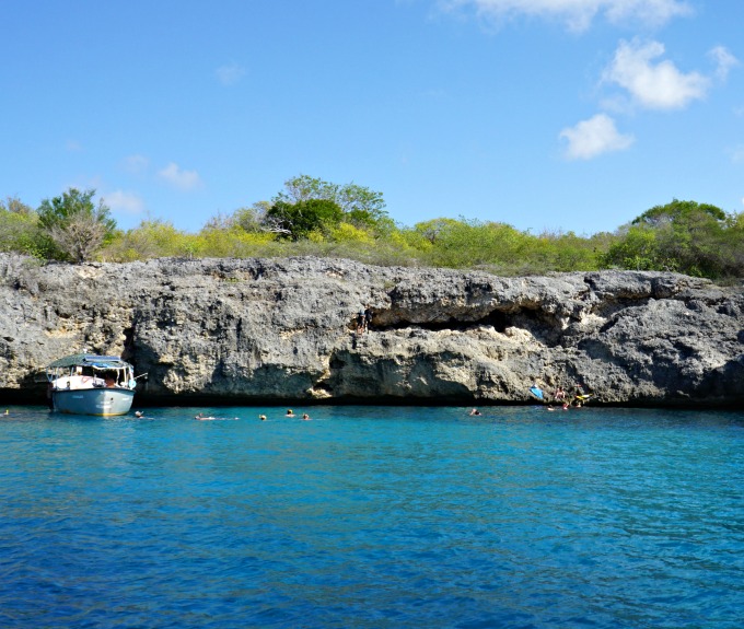 a coral rock cliff and deep blue waters with people swimming