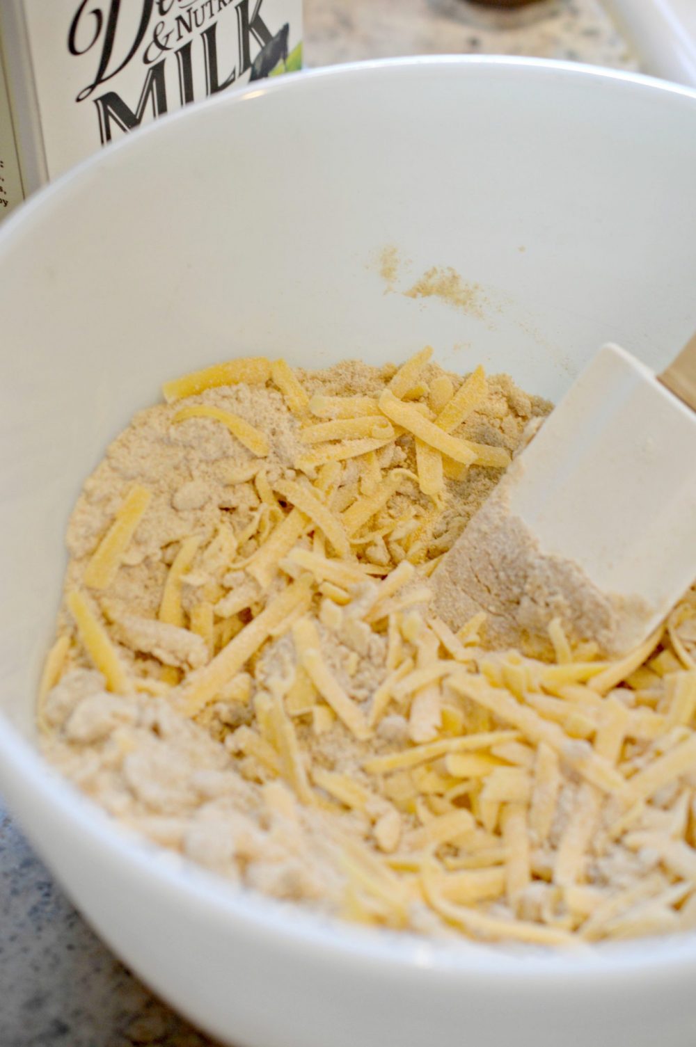 Adding shredded cheddar cheese to the flour and spices 