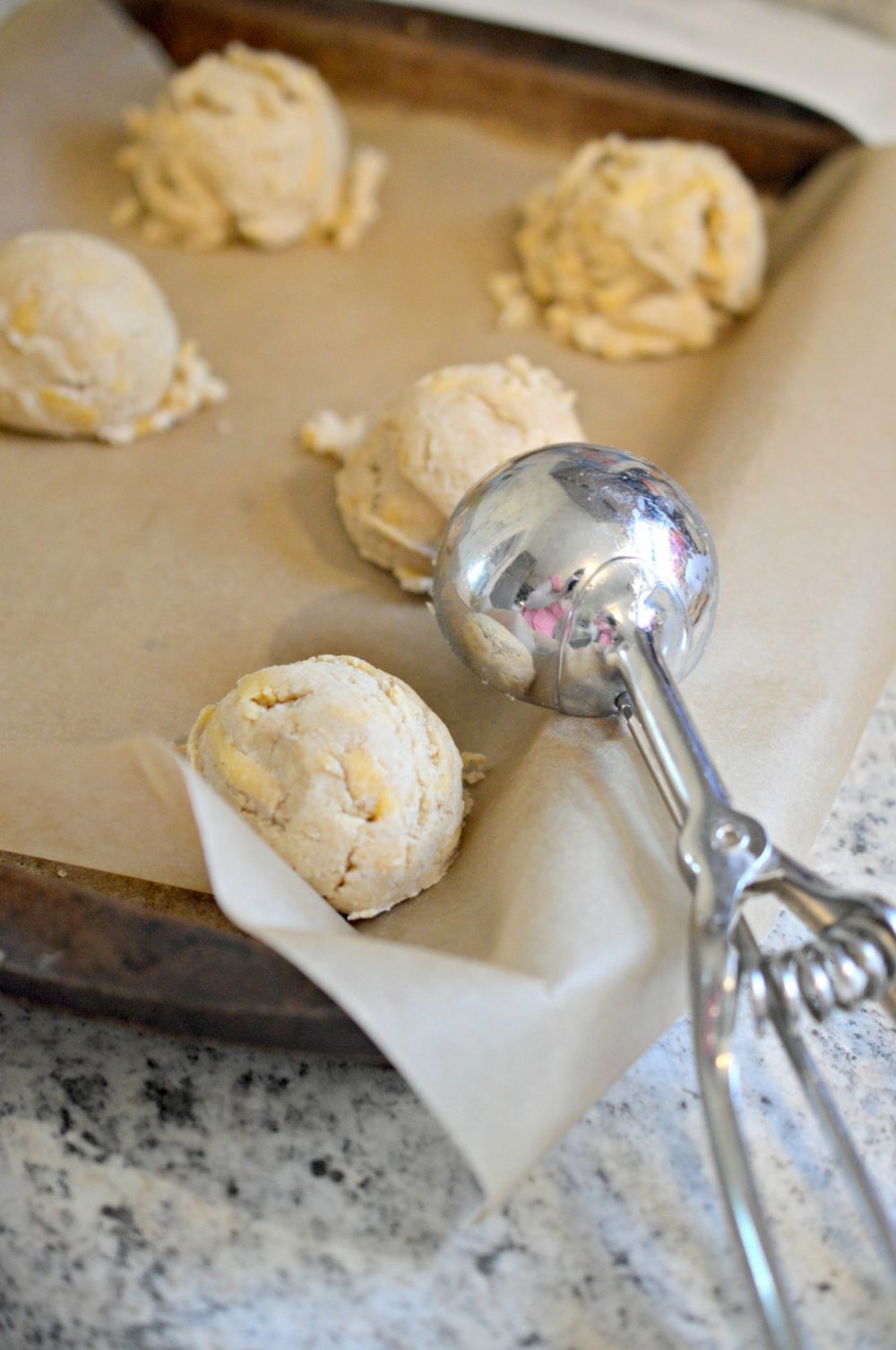 Using and ice cream scoop to place biscuit dough on a baking sheet 