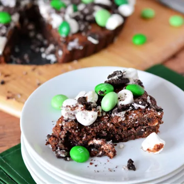 fudgy brownie covered in green candies and mini marshmallows on a wooden cutting board