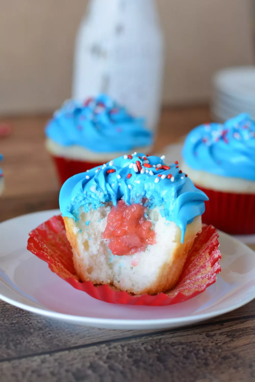 Vanilla cupcake filled with macerated strawberries and frosted with blue frosting and patriotic jimmies