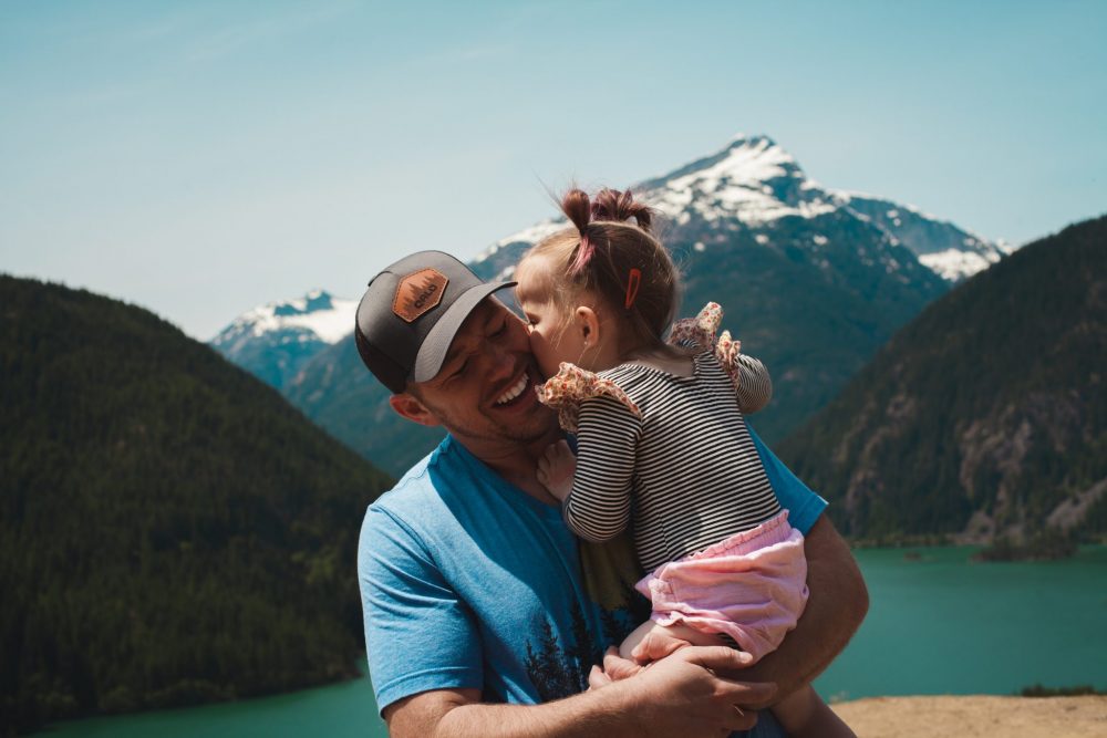 baby kissing daddy with the Alaskan mountains in the background
