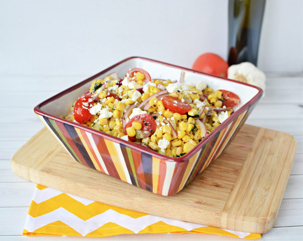  A bowl of corn and feta salad with tomatoes and onions.