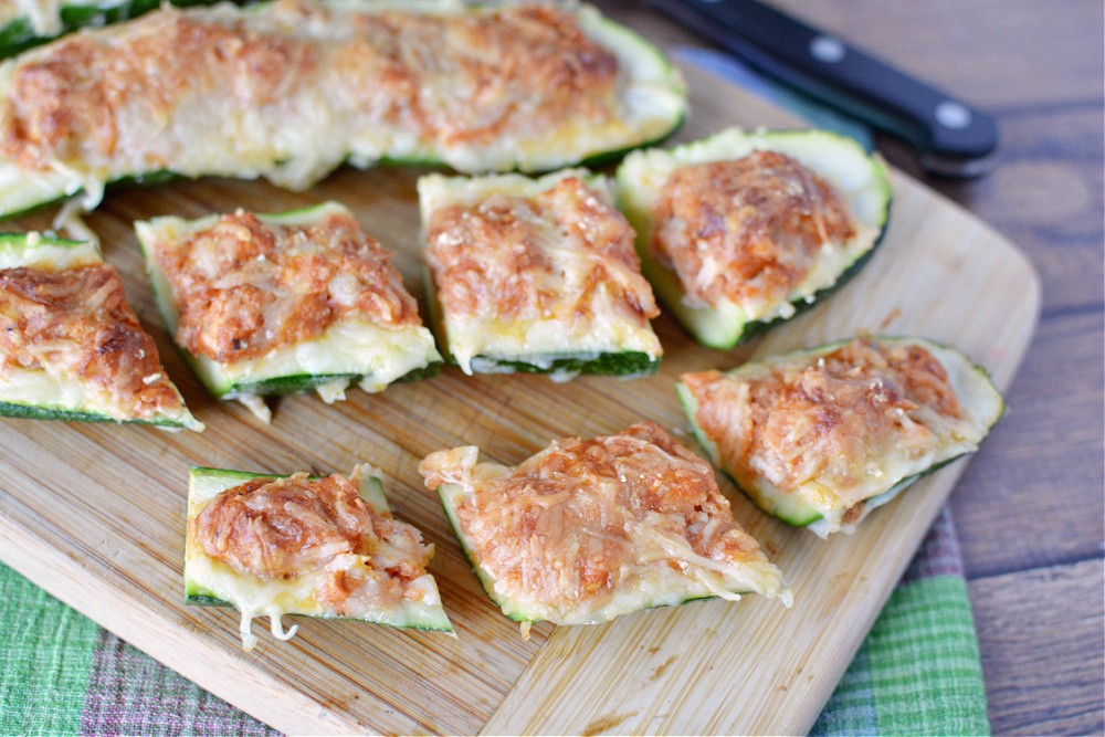 halved zucchini filled with ground beef or chicken and topped with melted cheese on a wooden cutting board