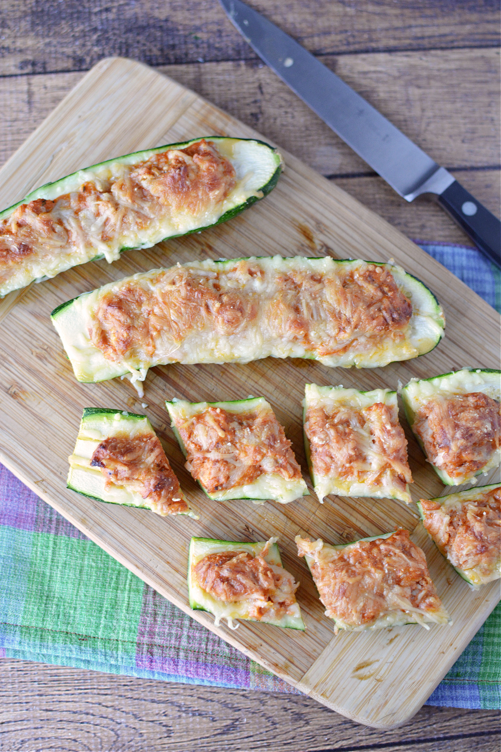 halved zucchini topped with melted cheese on a wooden cutting board