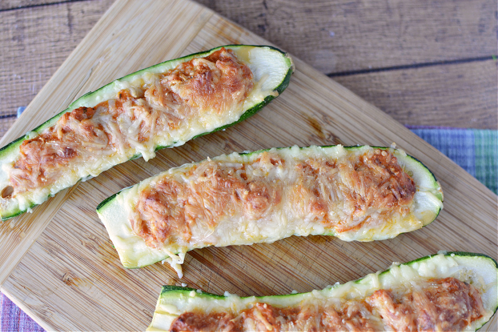 halved zucchini filled with ground beef or chicken and topped with melted cheese on a wooden cutting board