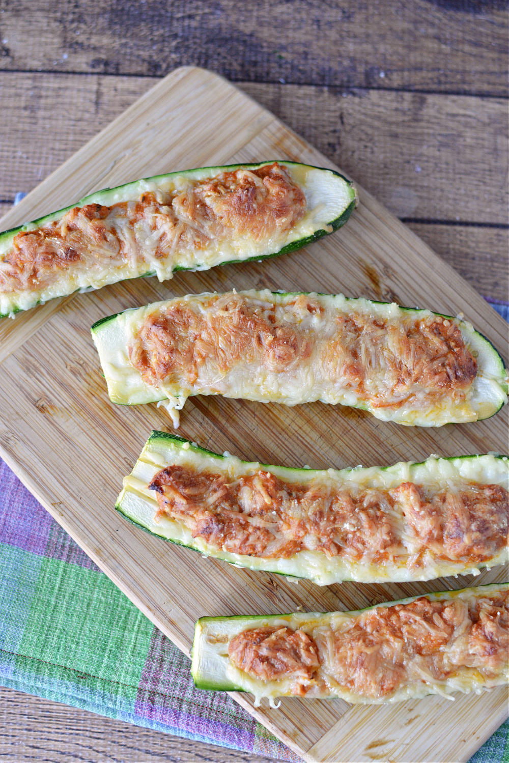 halved zucchini filled with ground beef or chicken and topped with melted cheese on a wooden cutting board