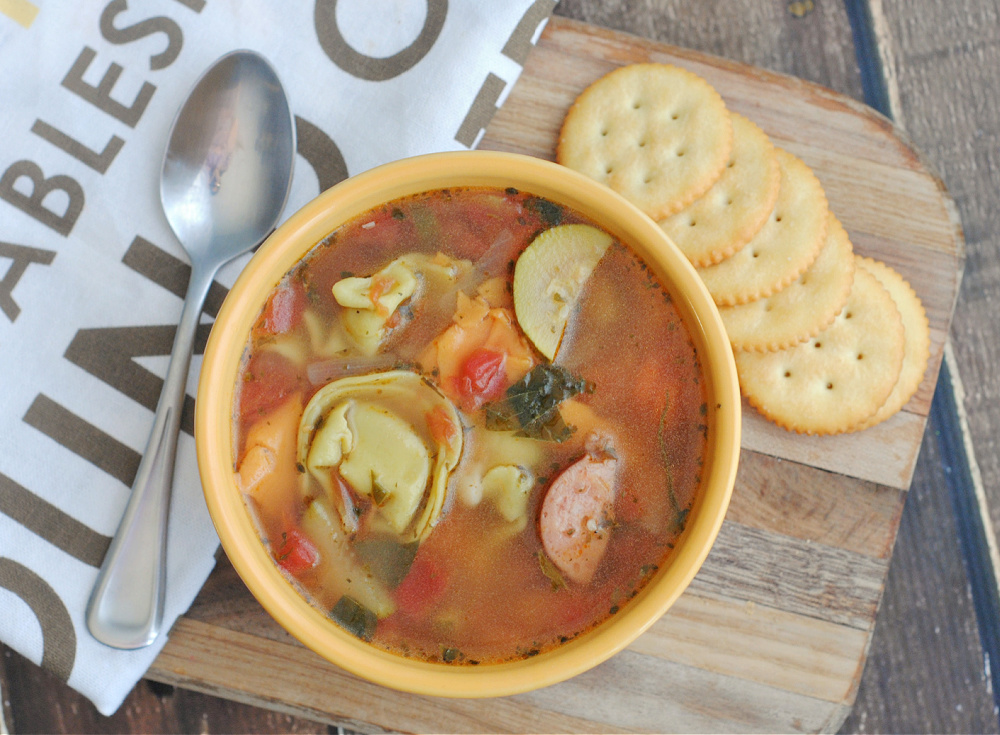 A bowl of soup with sausage and tortellini.