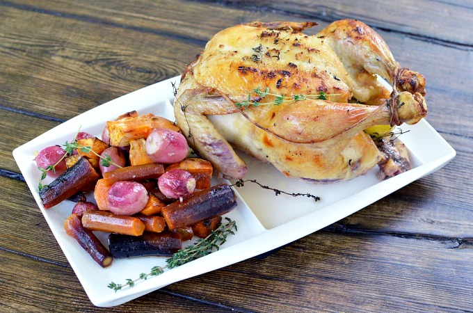 overhead shot of white serving platter with a whole roasted chicken and vegetables