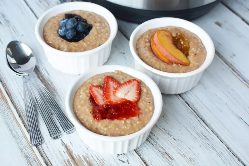 Oatmeal in white bowls with fresh strawberries, blueberries and peaches