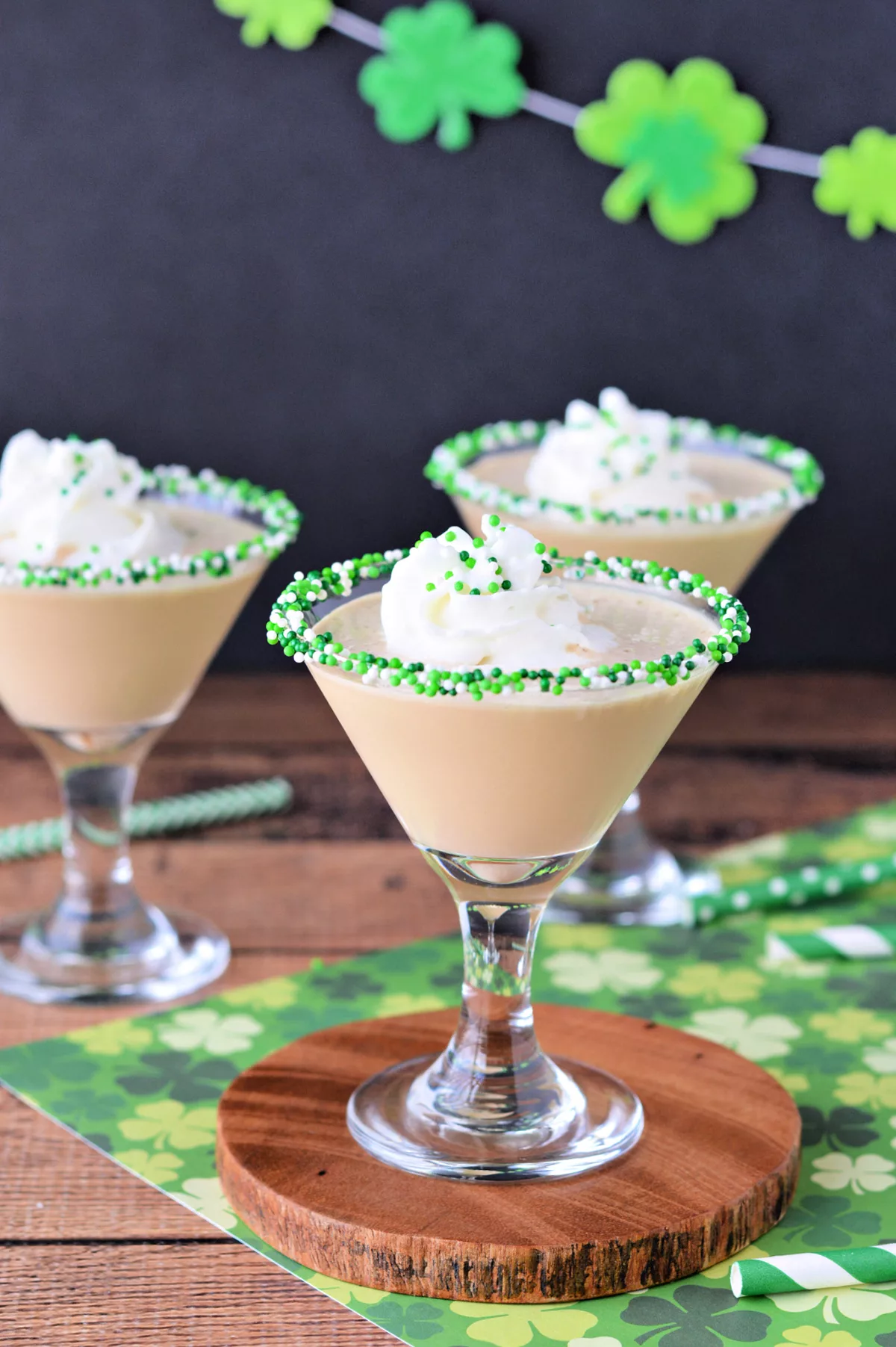 three martini glasses filled with baileys and topped with whipped cream and the rims are sprinkled with green sprinkles