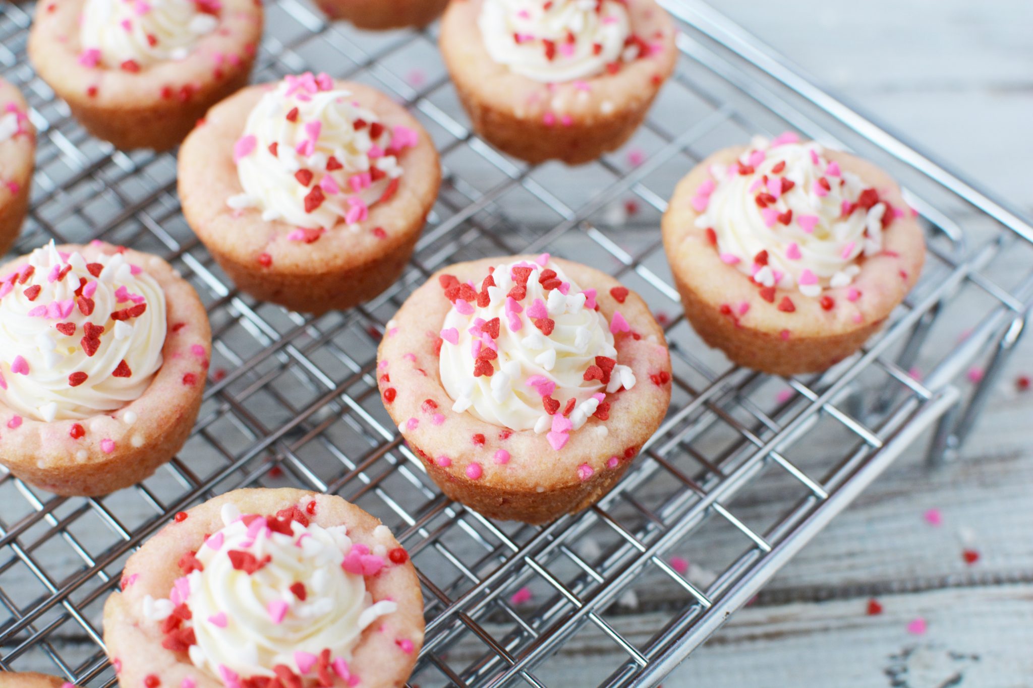Sugar Cookie Cups filled with frosting and covered with red and pink sprinkles sitting on stainless steel cooling racks