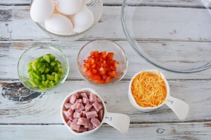 ingredients to make a quiche: diced ham, cheddar cheese, green peppers, red peppers and eggs