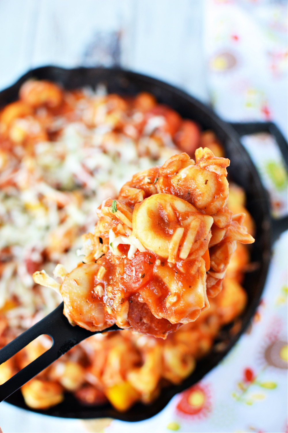 cast iron skillet filled with tomato sauce, tortellini pasta and covered in melted cheese