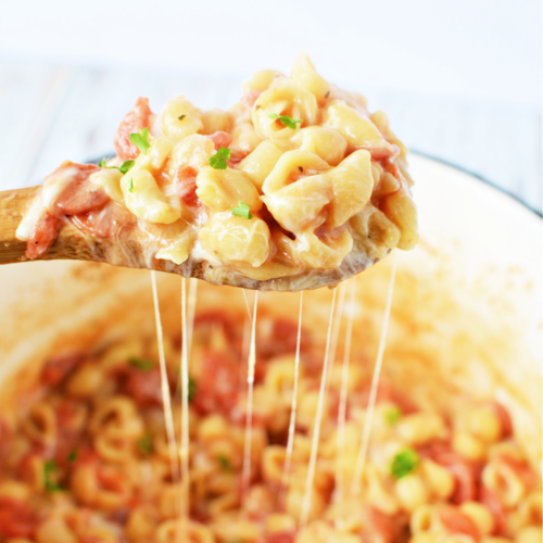 Wooden spoon filled with cheesy pasta and mini pepperonis over a pot of pizza pasta