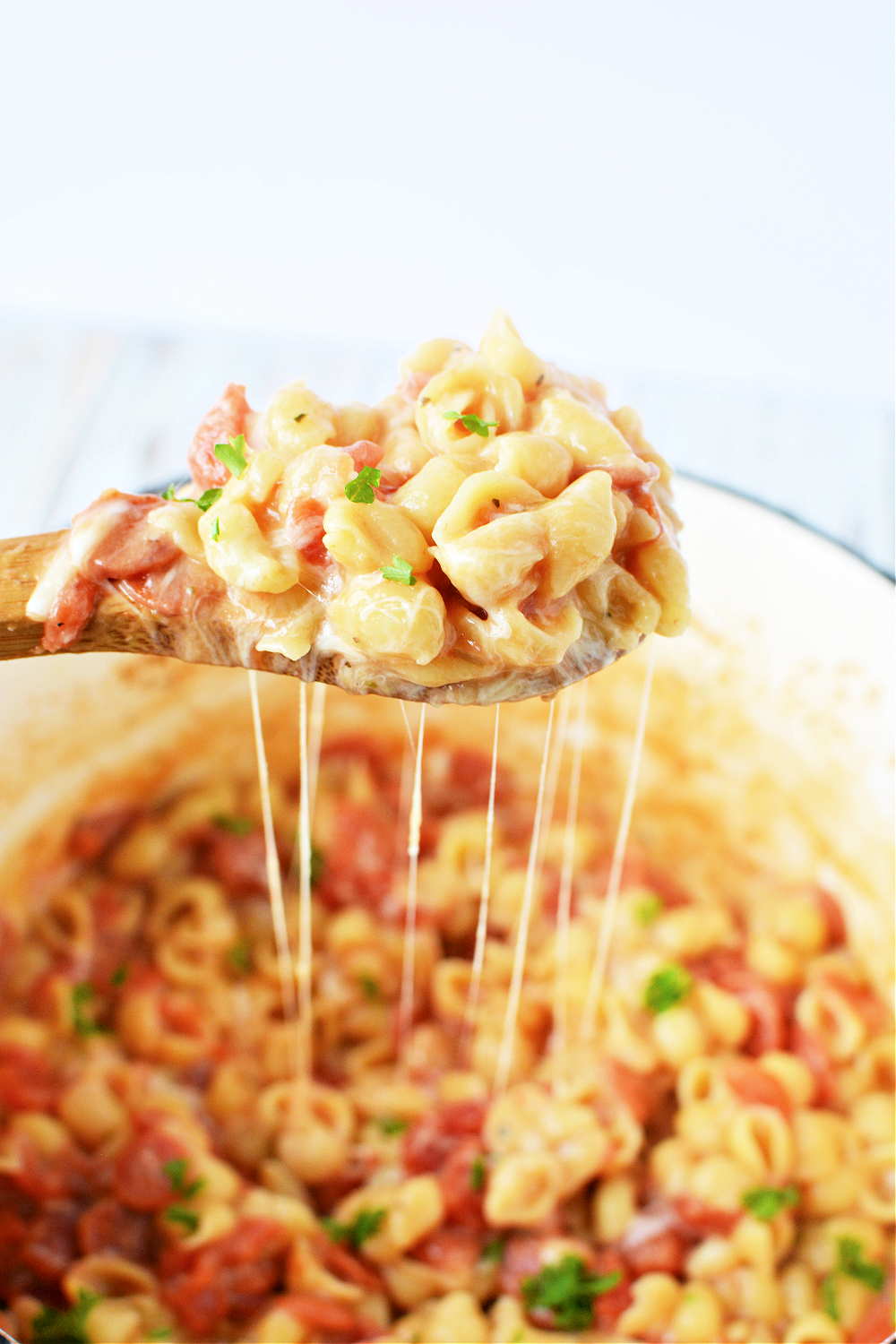 Wooden spoon filled with cheesy pasta and mini pepperonis over a pot of pizza pasta