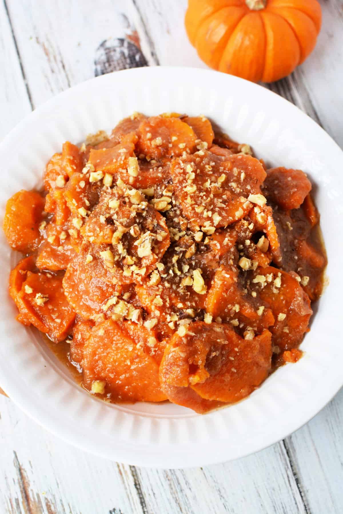 white bowl filled with sweet potatoes and apple sauce topped with chopped pecans