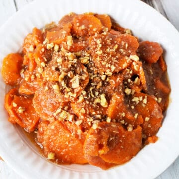 white bowl filled with sweet potatoes and apple sauce topped with chopped pecans