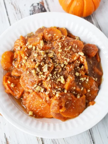 white bowl filled with sweet potatoes and apple sauce topped with chopped pecans