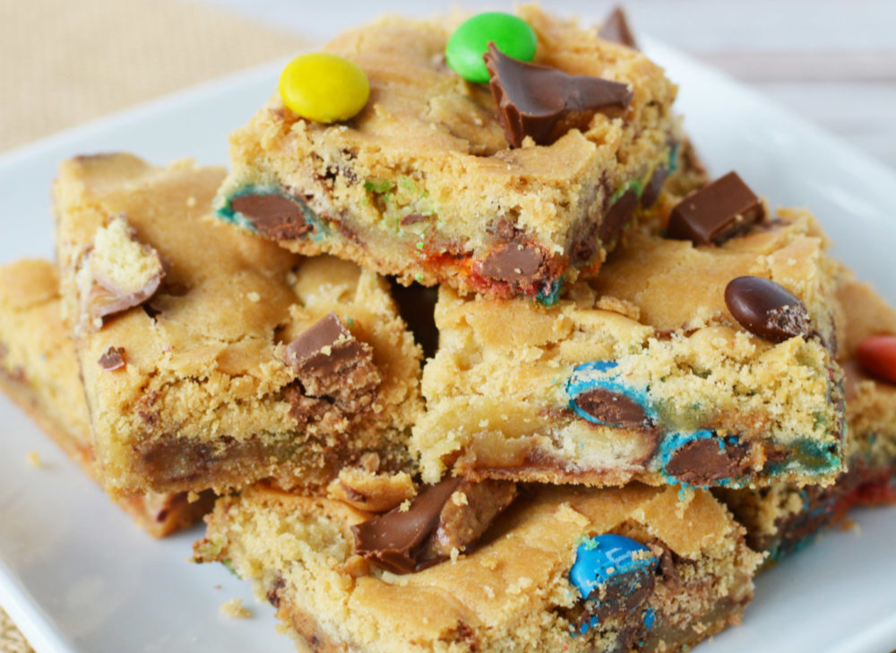 Candy Cookie Bars stacked on a plate full of pieces of chocolate candy