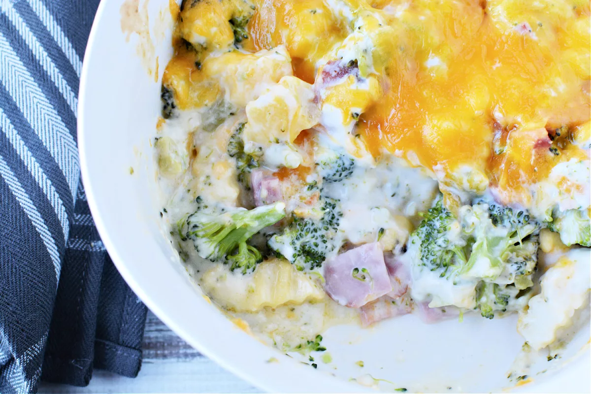 white dish filled with broccoli florets, chunks of ham, french fries and cheese melted on top