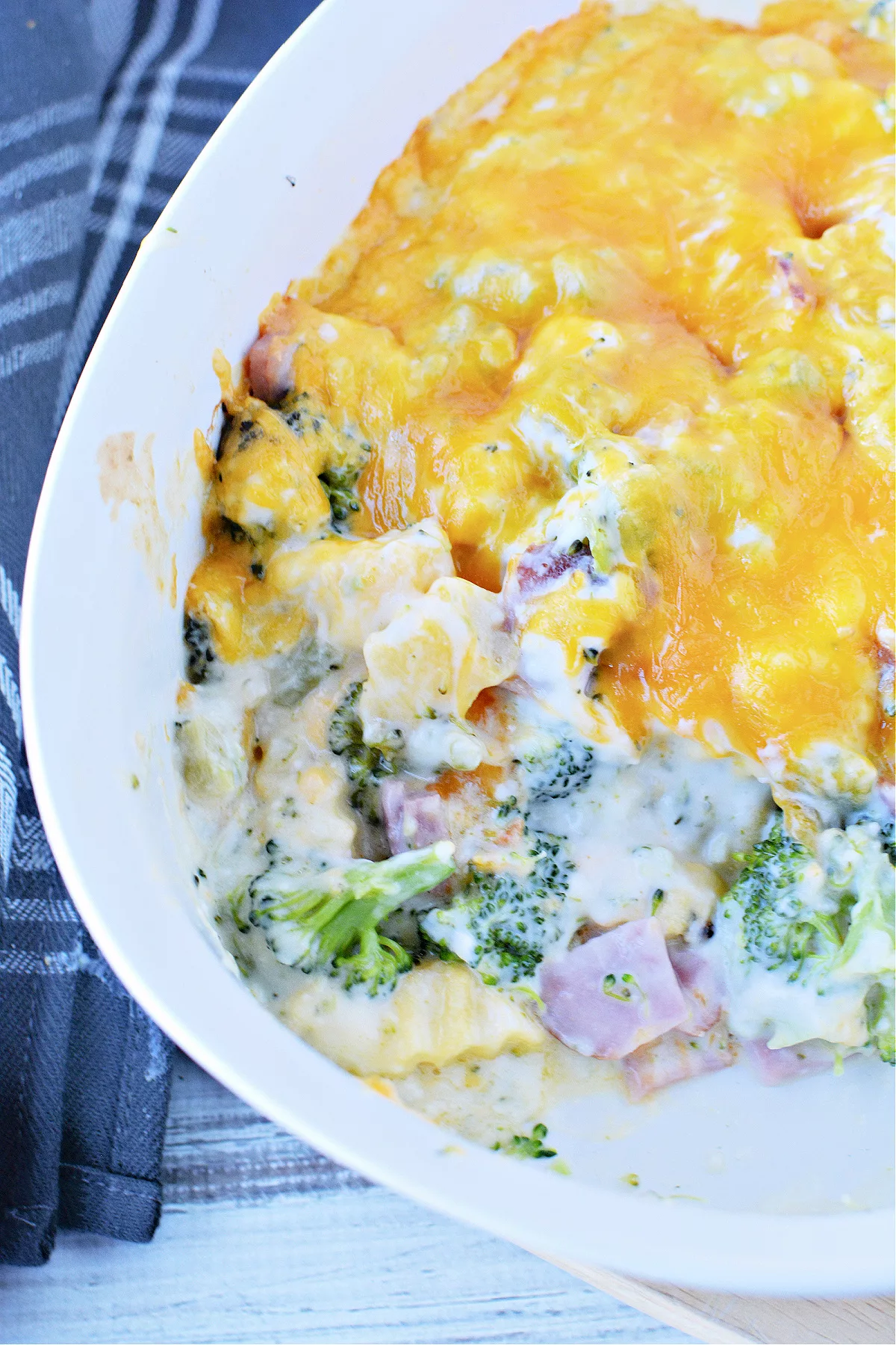 white dish filled with broccoli florets, chunks of ham, french fries and cheese melted on top