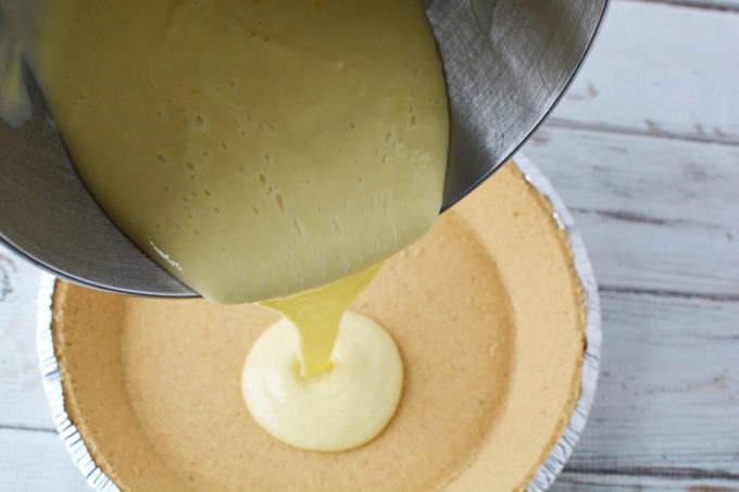 Pouring lemon pie filling on top of a graham cracker crust 