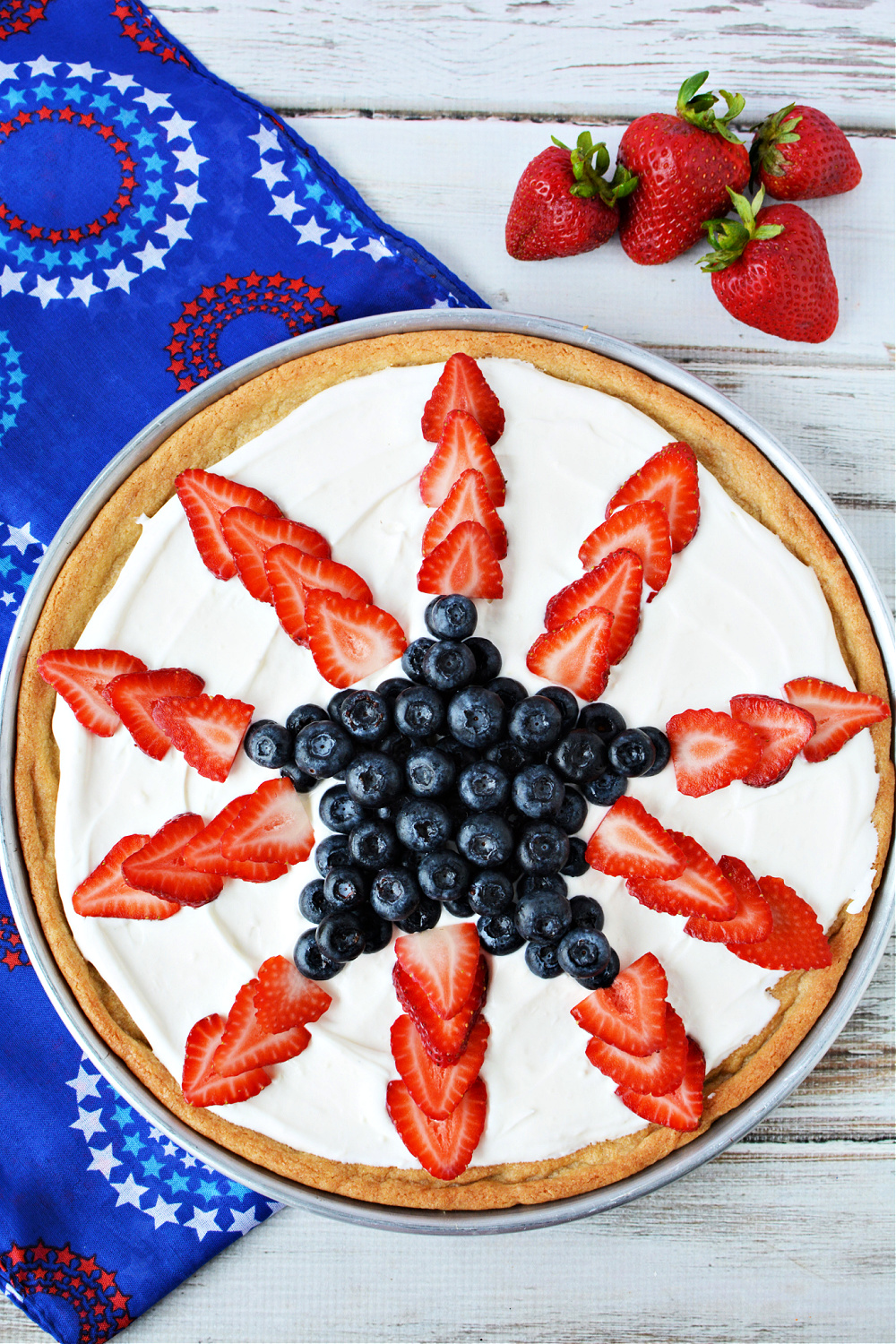 pizza made out of cookies with white whipped topping and sliced strawberries and blueberries