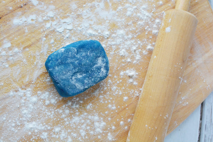 blue cookie dough on a cutting board with flour and a rolling pin
