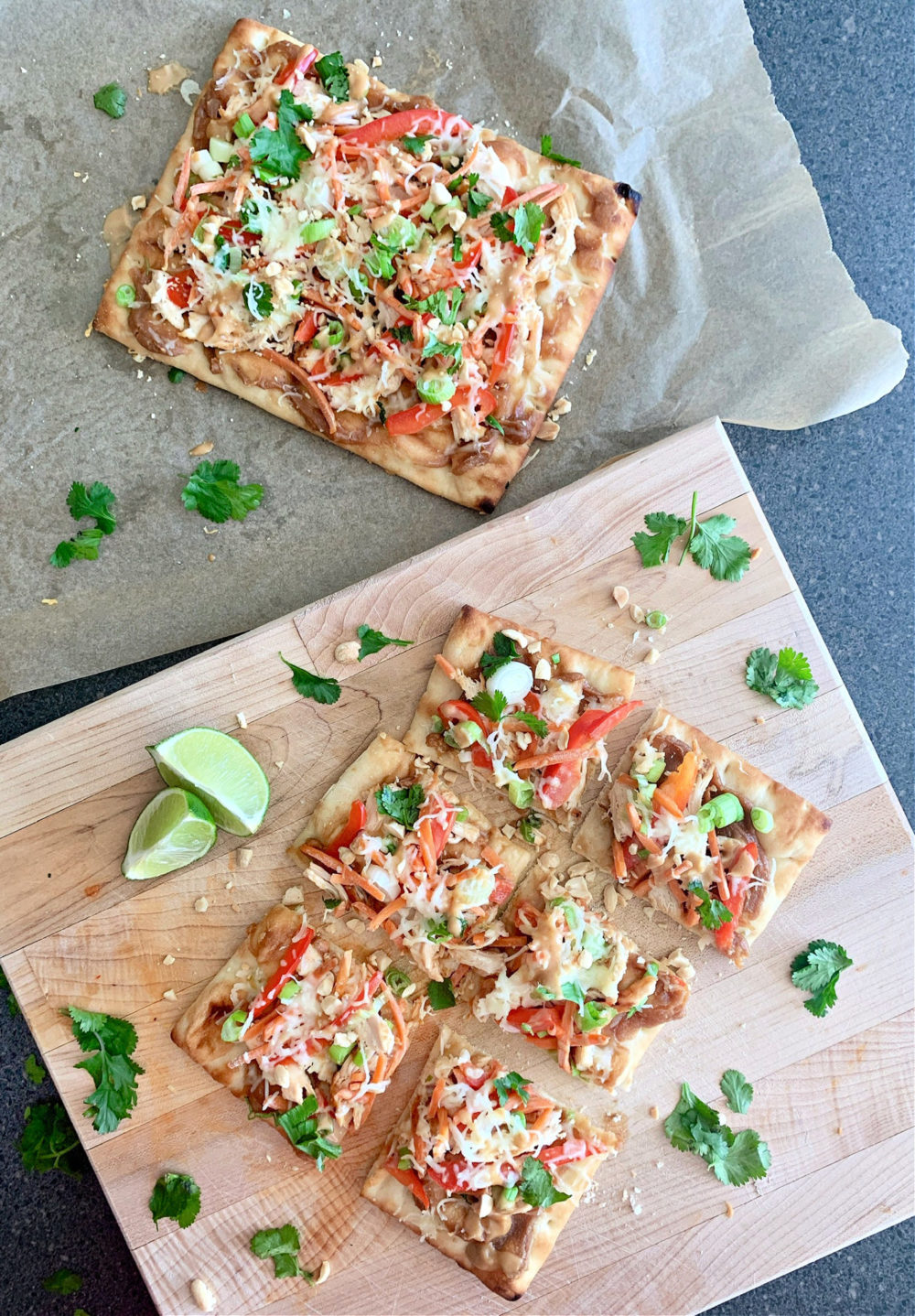 thai chicken pizza covered in chicken and veggies and cheese on a plate with lime wedges