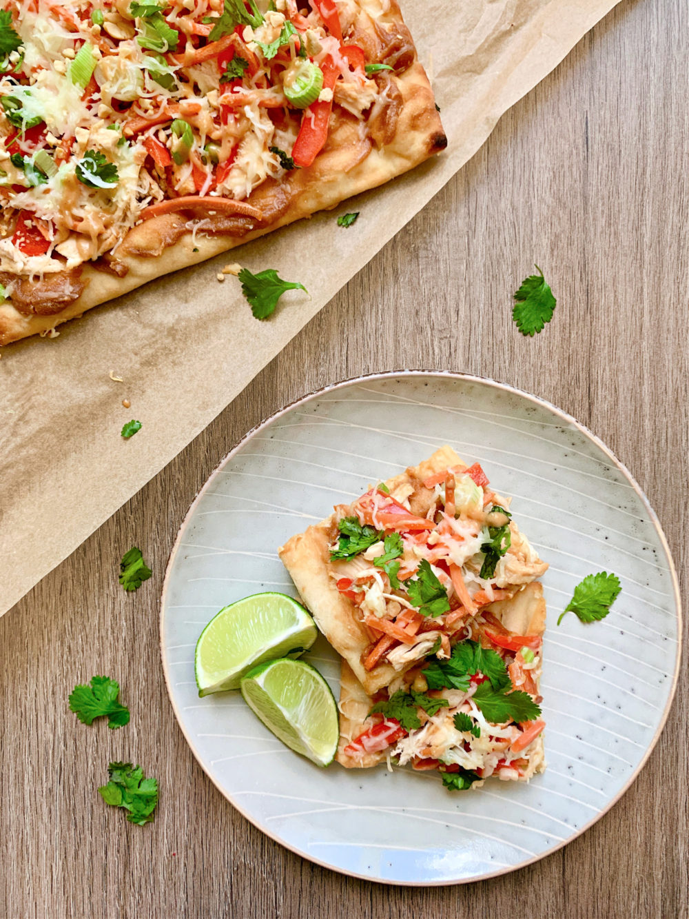 thai flatbread pizza covered in chicken and veggies and cheese on a plate with lime wedges