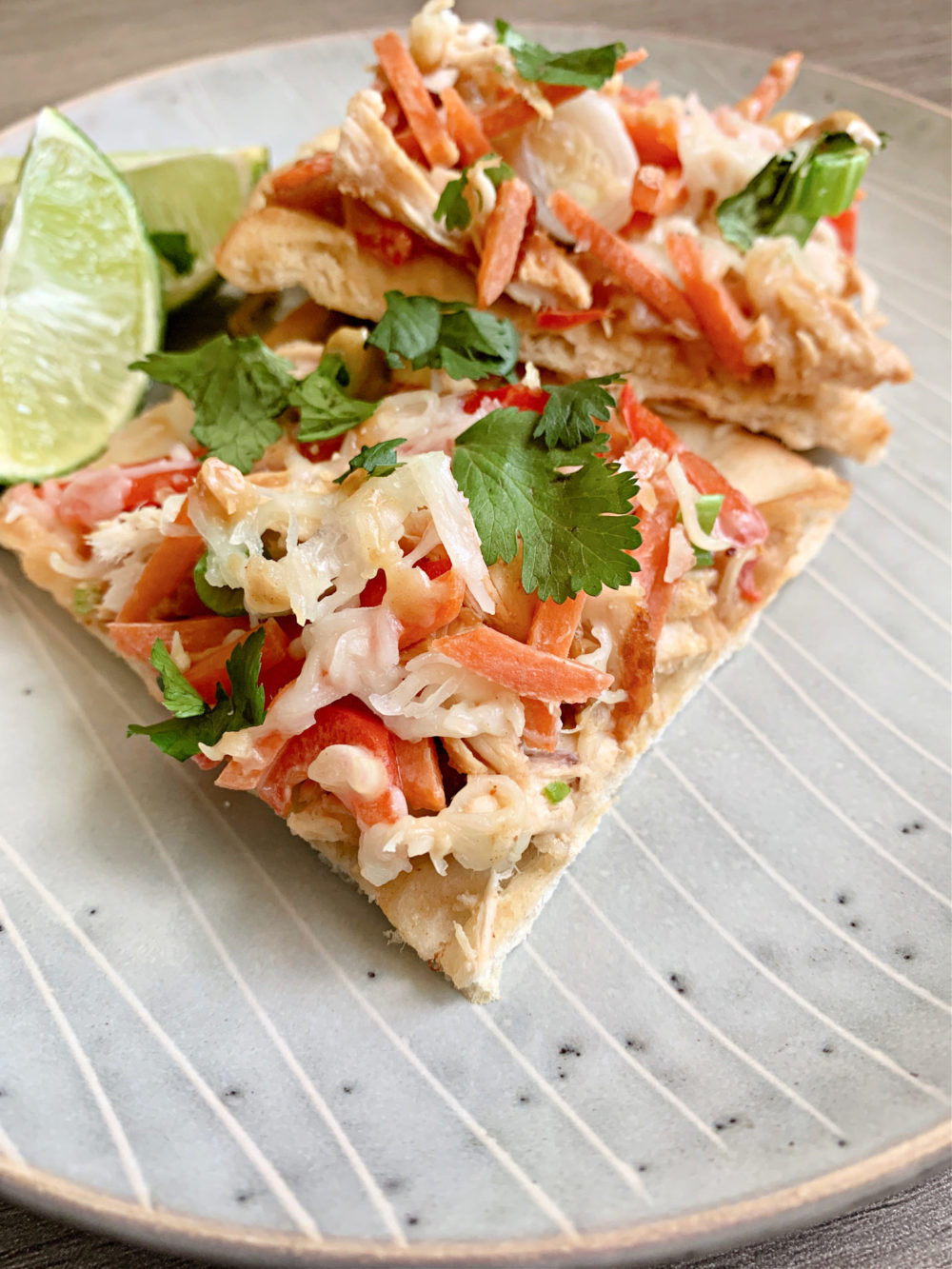 Thai Chicken Pizza flatbread covered in chicken and veggies and cheese on a plate with lime wedges
