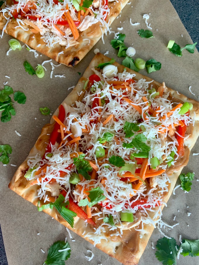 Thai Chicken Pizza flatbread covered in chicken and veggies and cheese on a plate with lime wedges