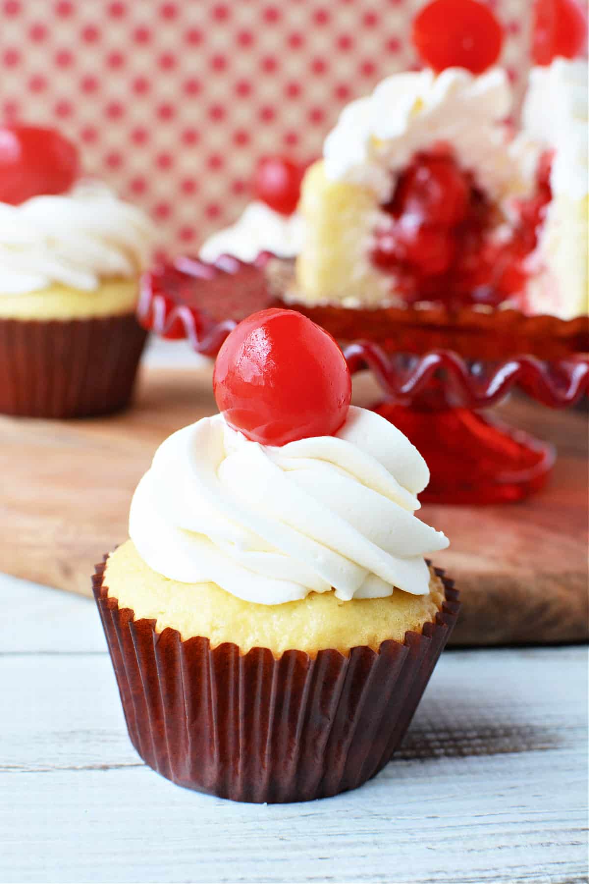 Cherry Filled Cupcakes on a plate with homemade vanilla buttercream frosting and topped with a single maraschino cherry
