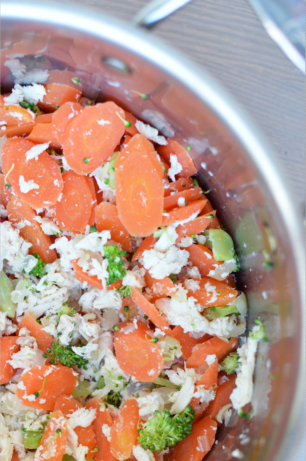 close up shot of pot filled with shredded chicken, sliced carrots, broccoli