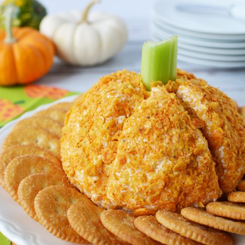 Cheese Ball shaped like a pumpkin with crushed orange doritos all over it and a celery stalk as a stem
