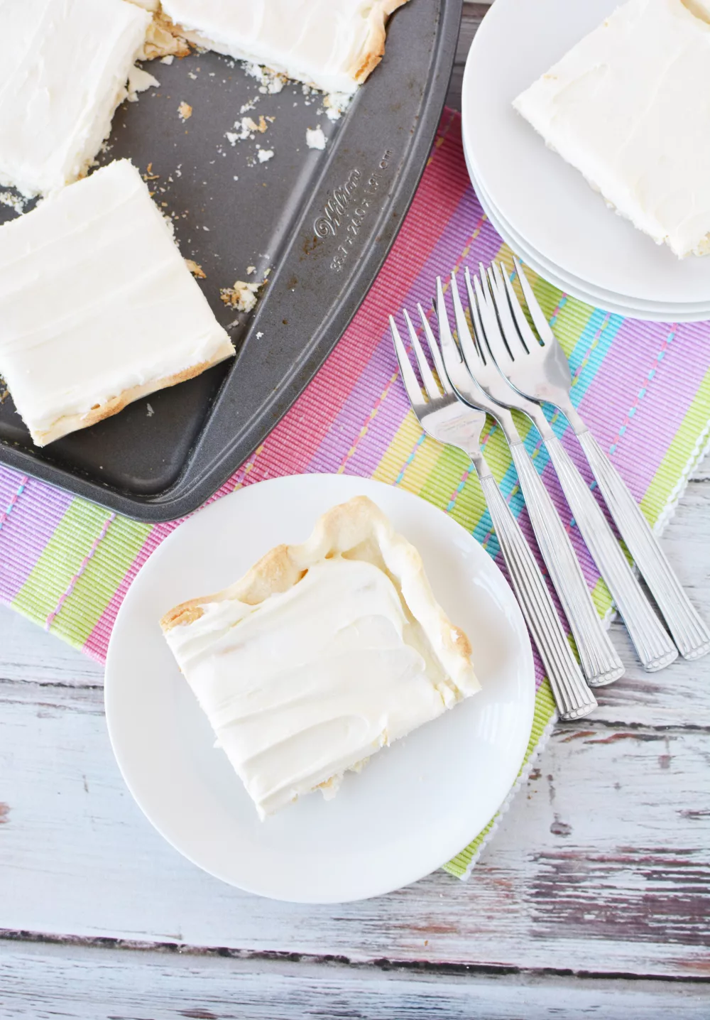 cheese cake served on white plates with colorful napkins and forks on the table