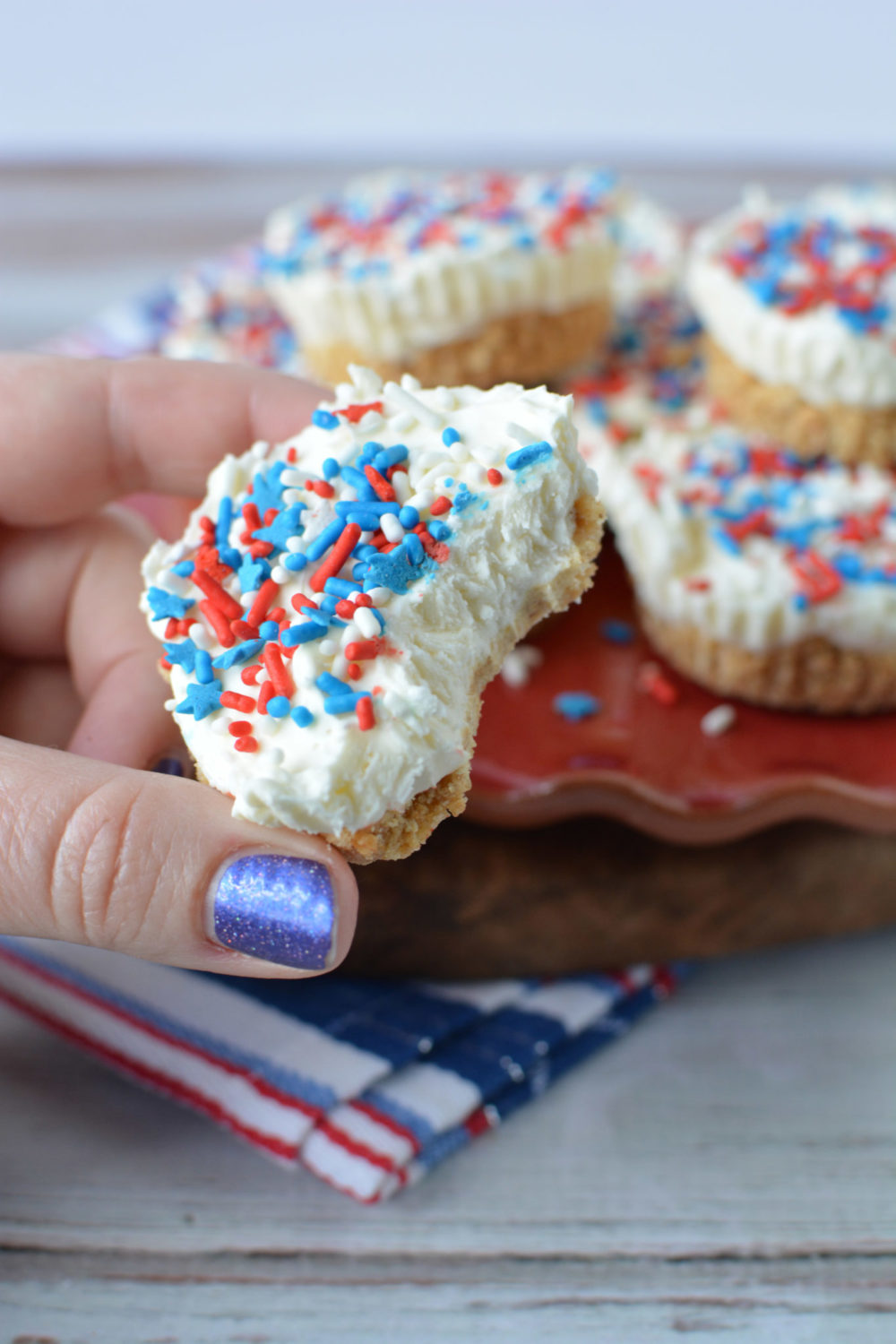 A hand holding a mini cheesecake that is decorated with red and blue sprinkles 