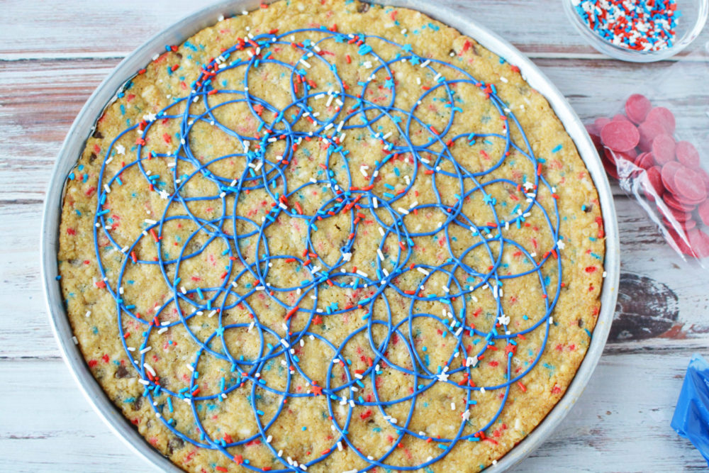 Drizzling blue candy melts all around the baked cookie