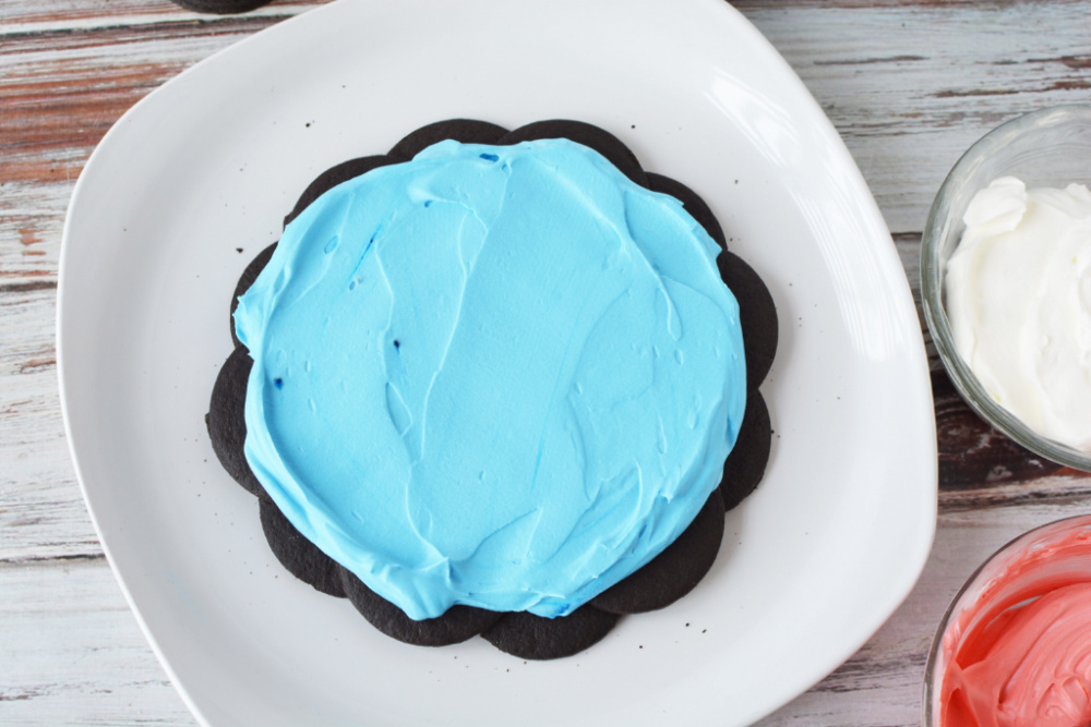 Adding blue whipped cream on top of the chocolate wafer cookies 