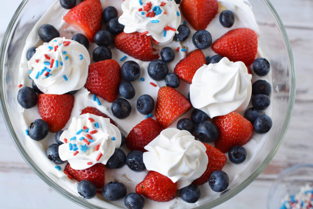A close-up of the top of a strawberry and blueberry trifle with dollops of whipped cream on top